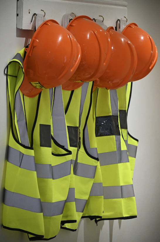 Hard hats and neon reflective vests on hooks.